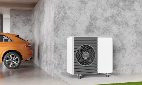 Wärmepumpe an Häuserwand. Im Hintergrund ein Auto